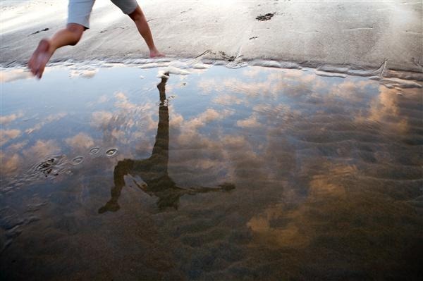 Women Leaping over Puddle on Beach